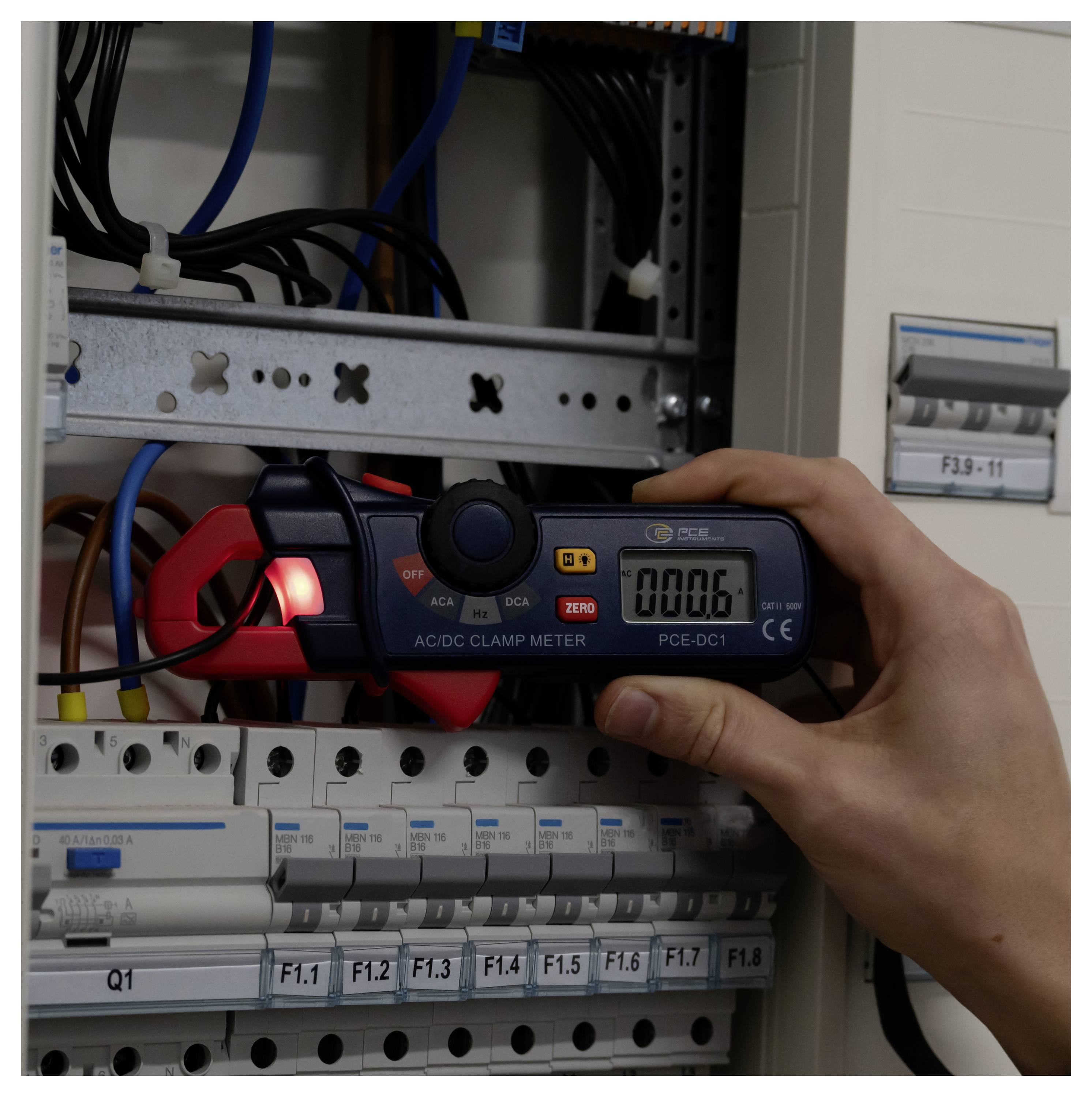 Oseba, ki uporablja digitalni AC/DC sponko meter za merjenje napeljave znotraj elektrika preklopnega panela.