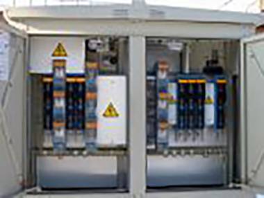 Odprta električna omarica prikazuje več elektronskih komponent in kablov z opozorilnimi simboli.