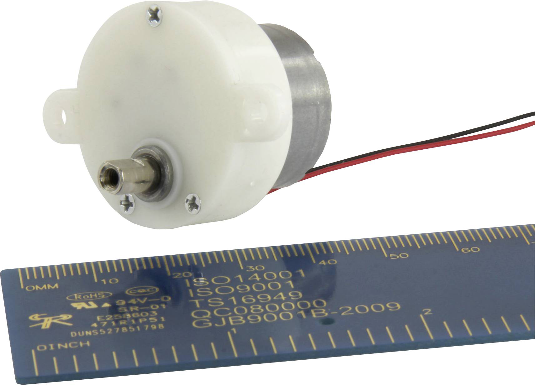 Mali elektromotor s kovinskim ohišjem in plastičnim pokrovom, zraven ravnilo za določanje velikosti.