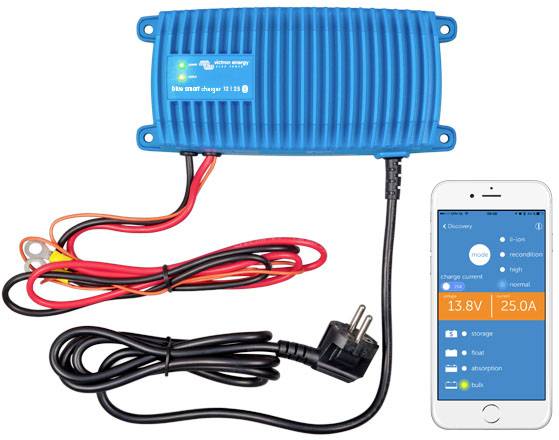 Modra polnilna naprava za baterije z rdečimi in črnimi kabli, priključena v električno vtičnico. Pametni telefon prikazuje parametre polnjenja: 13,8 V, 25,0 A.