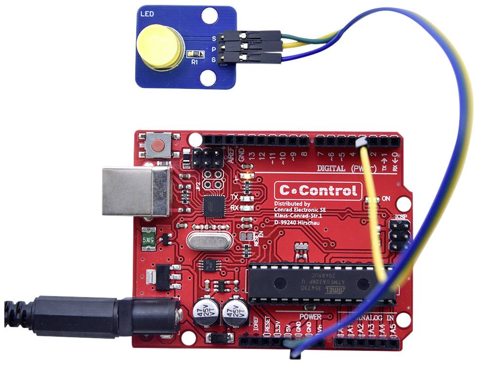 Rdeča mikrokontrolna plošča z USB-portom in modrim LED-senzorskim modulom, povezana z žico, prikazuje elektronsko vezje.