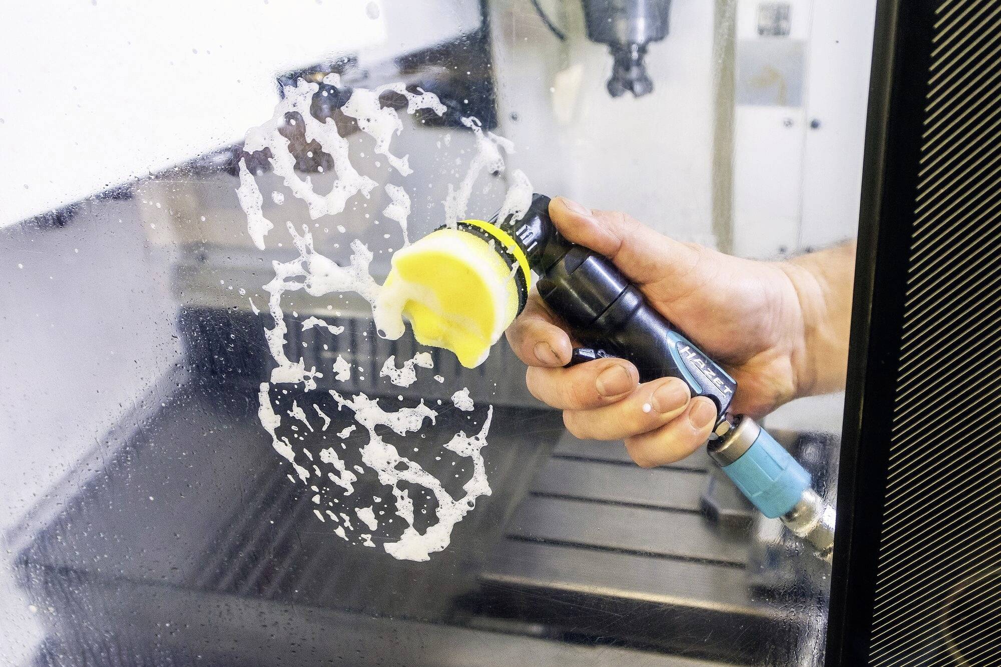 Ena roka drži rotirajoče polirno orodje in odstranjuje ostanke mila s steklene površine v delavniškem okolju.
