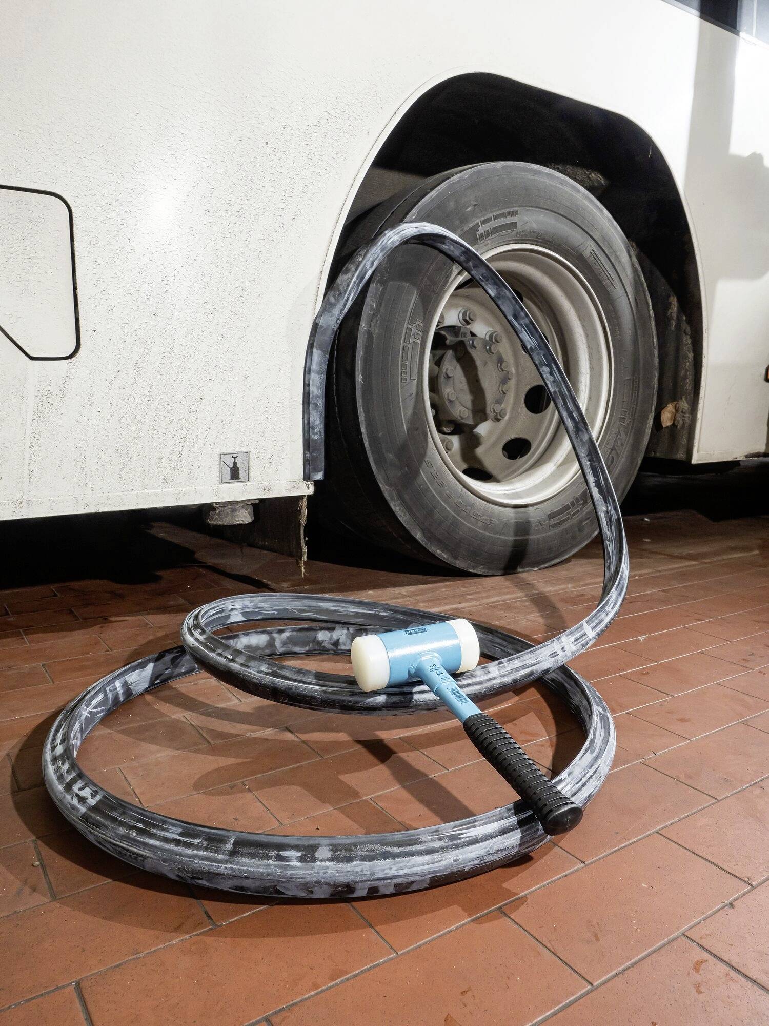Avtobusna pnevmatika z poškodovano gumo, ki leži sproščeno na tleh. Kladivo leži na gumi.