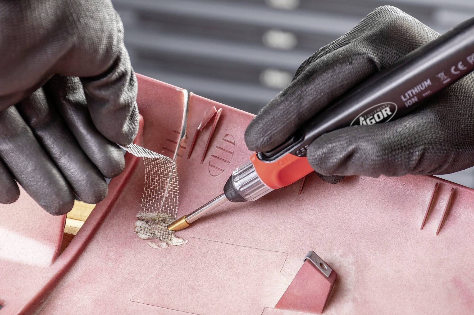 Oseba z spajkalnikom obdeluje rdeč plastičen del, da bi popravila poškodovan kos s področjem ojačitve.