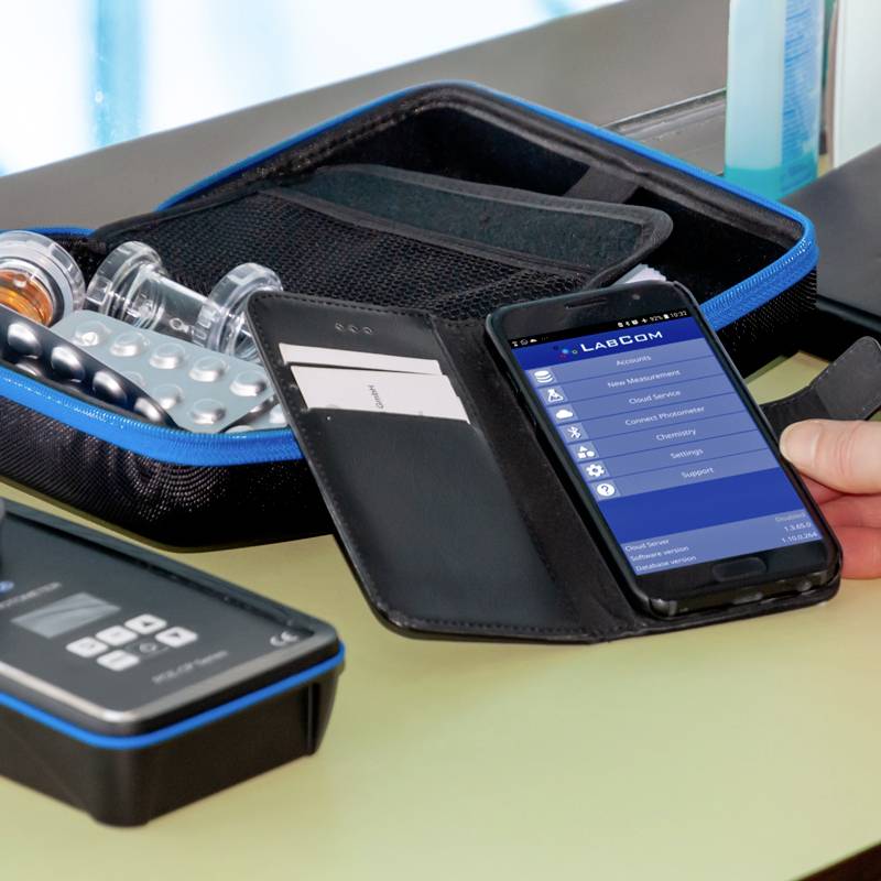 Pametni telefon prikazuje odprto aplikacijo z možnostmi. Zraven leži etui z tabletami in dve steklenički.