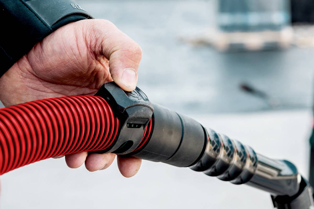 Oseba drži rdečo električno polnilno šobo in prikazuje postopek polnjenja vozila.