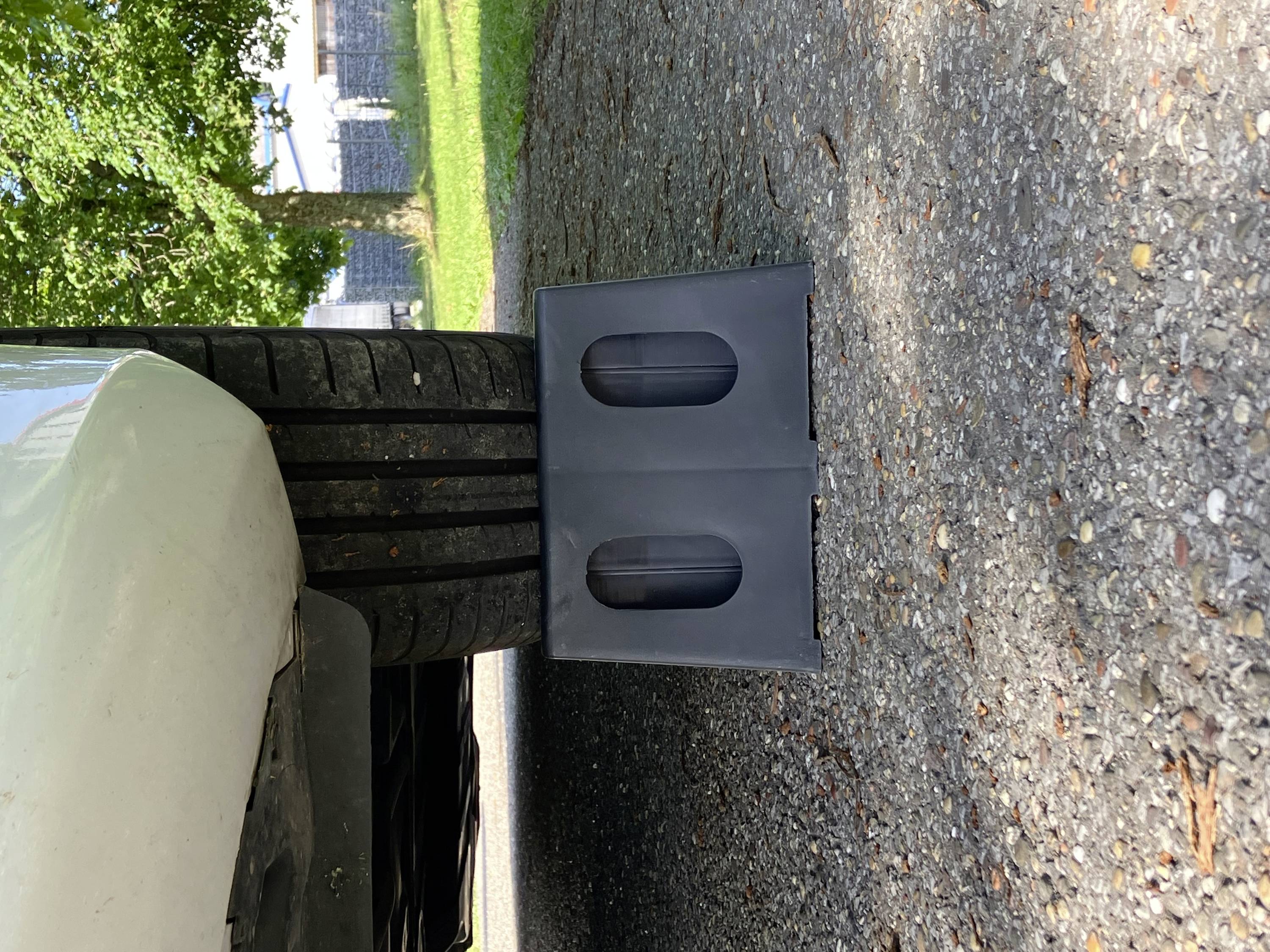 Avto parkiran na dvižni ploščadi za lažjo menjavo pnevmatike; pnevmatika je delno dvignjena. V ozadju trava in drevesa.