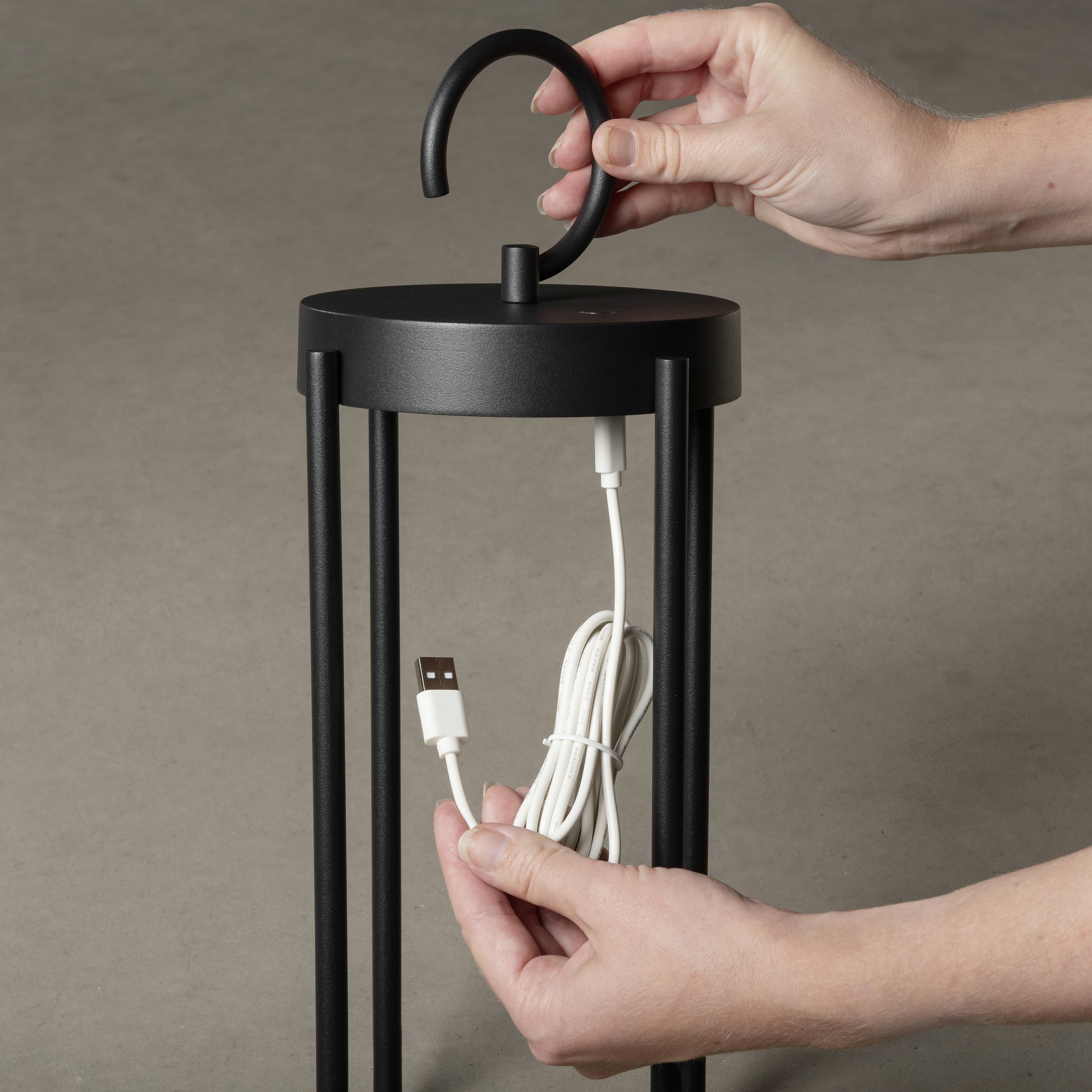 Oseba drži črno, cilindričnega oblike napravo z zanko v eni roki in zvit USB-kabel v drugi roki.