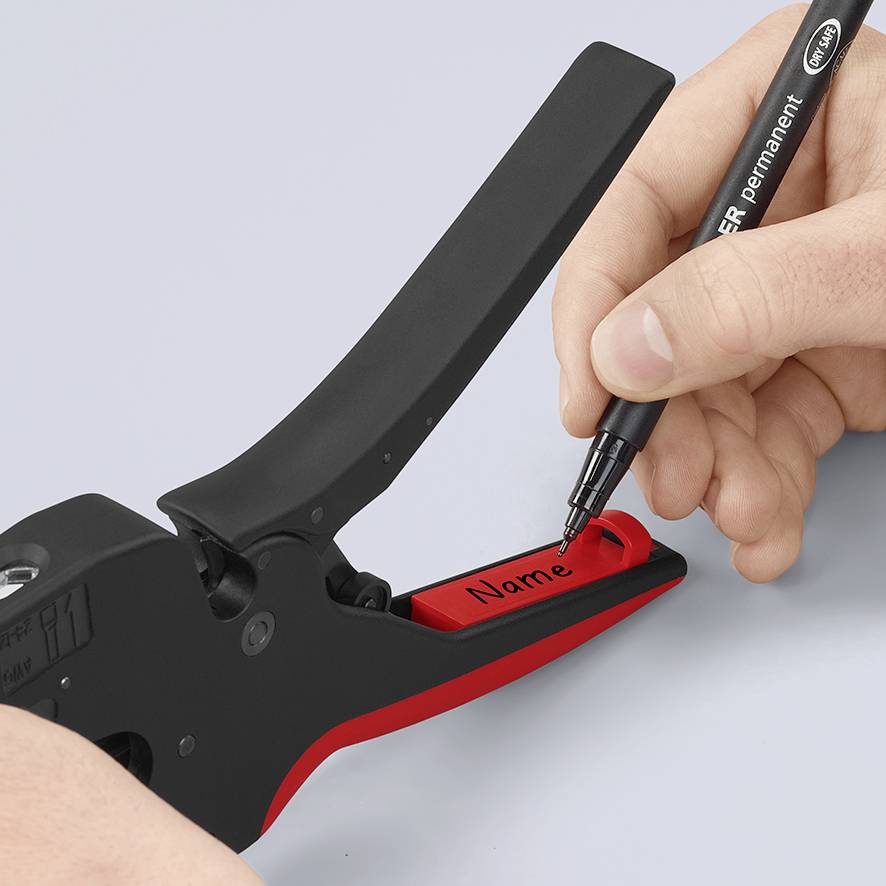 Roka s črnim svinčnikom piše po rdečem imenskemuoznaki, ki je vpeta v napravo za izdelavo nalepk.