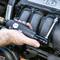 Oseba z električnim vijačnikom zategovuje vijake na motorju avtomobila. V ozadju je vidna pokrov motorja 1.6.