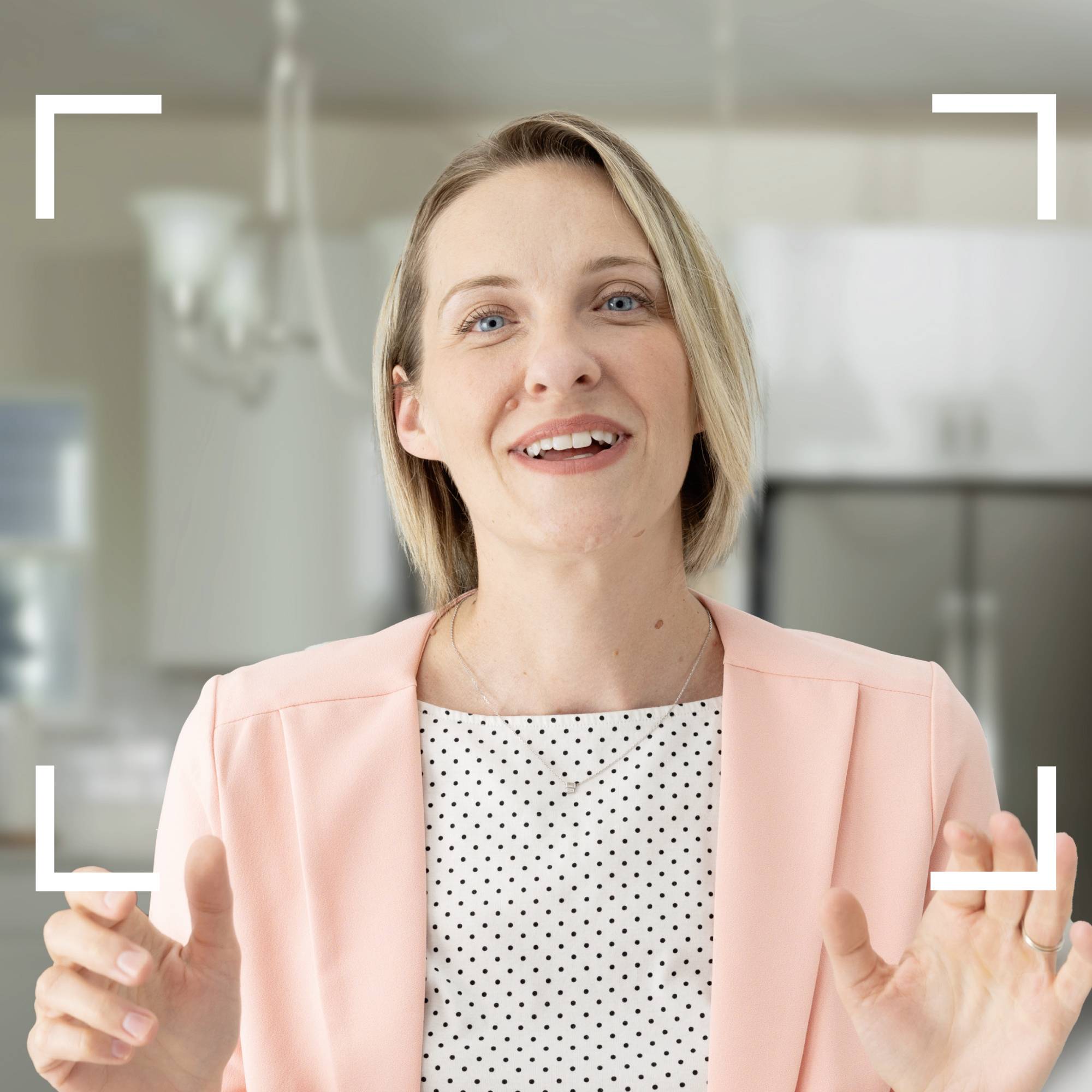 Nasmejana oseba v rožnatem blazerju stoji v sodobno urejeni sobi.