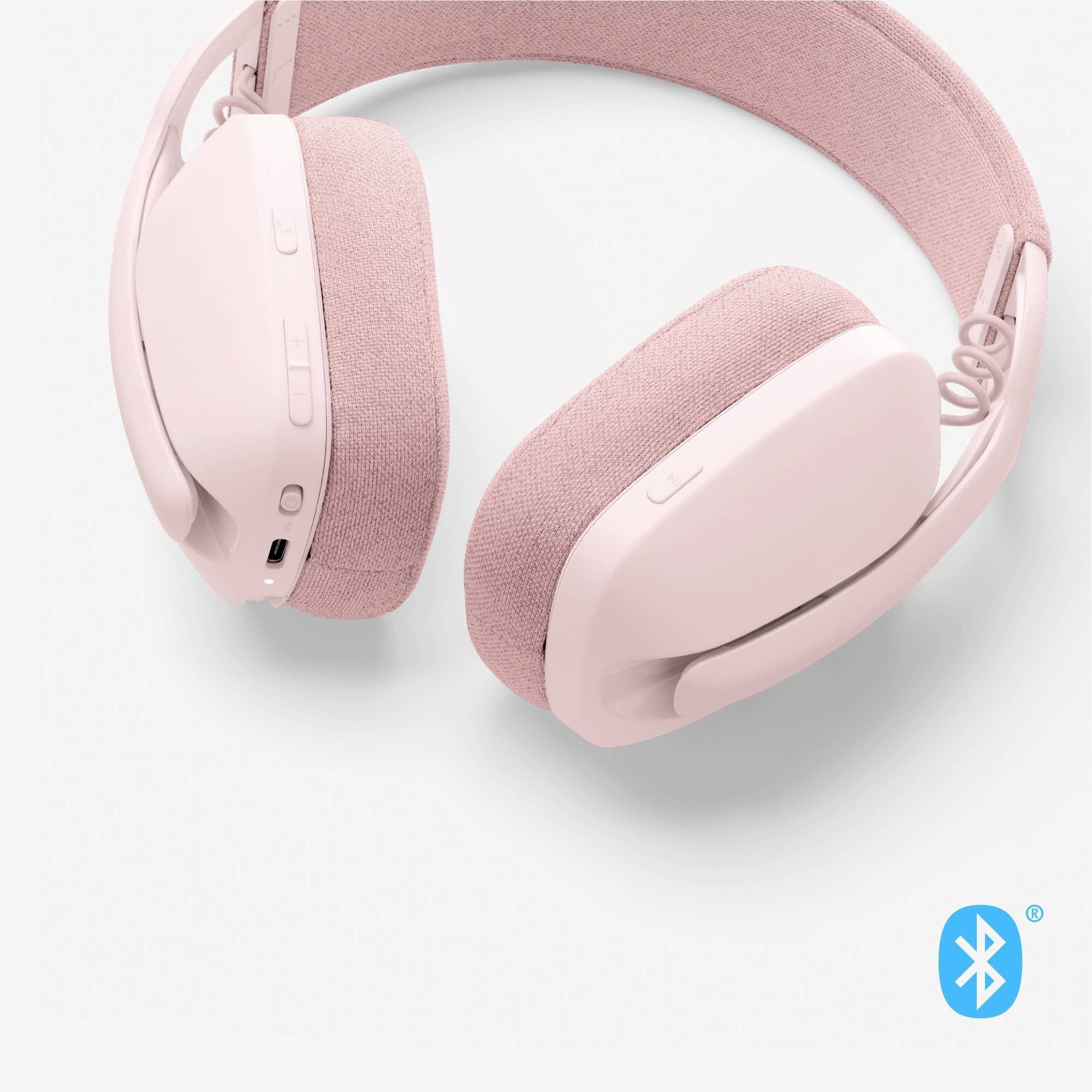 Brezžične, rožnate bluetooth slušalke z mehkimi ušesnimi blazinicami in tipkami za upravljanje ob strani.
