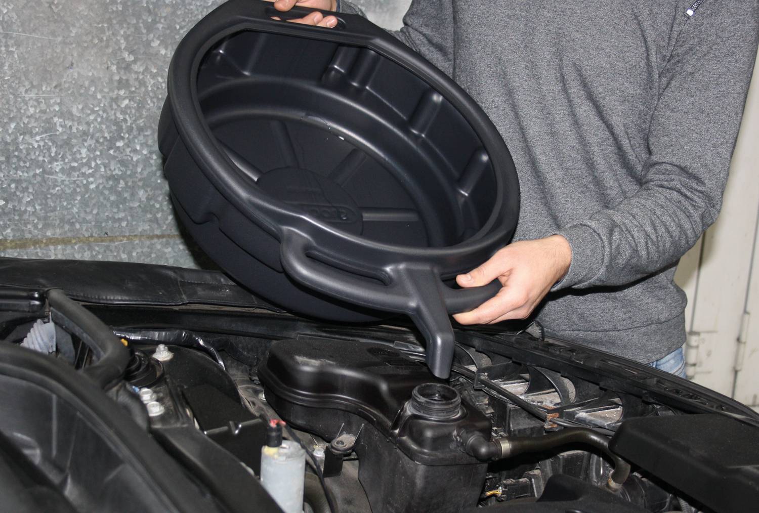 Oseba menja olje pri avtomobilu in uporablja črno posodo za prestrezanje starega motornega olja.