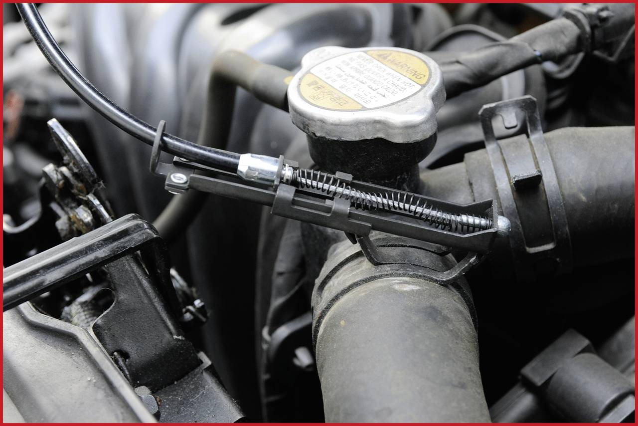 Avtomobilski motor z odprtim pokrovčkom hladilnika. Cev s kovinsko sponko je vidna, obdana z kovinskimi in plastičnimi deli.