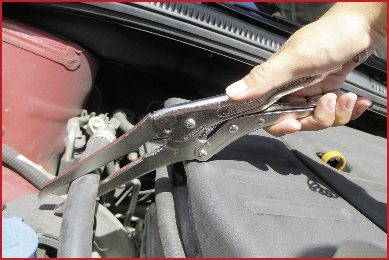 Ena roka drži klešče, ki stiskajo cev pod pokrovom motorja avtomobila.