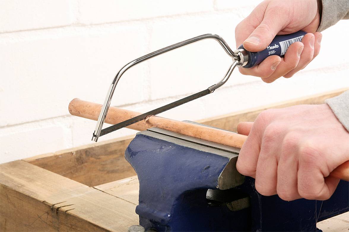 Oseba z mehansko žago reže bakreno cev, pritrjeno v čeljustih imenske stege.