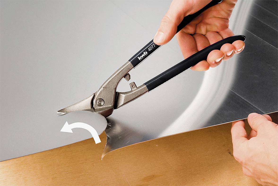 Roka uporablja kovinske škarje za rezanje pločevine vzdolž krivulje.