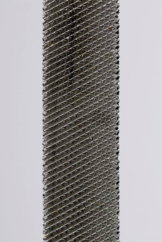 Bližnji posnetek kovinske pile s fino mrežasto teksturo in sivo barvo. Pomembno orodje za natančno brušenje in oblikovanje.