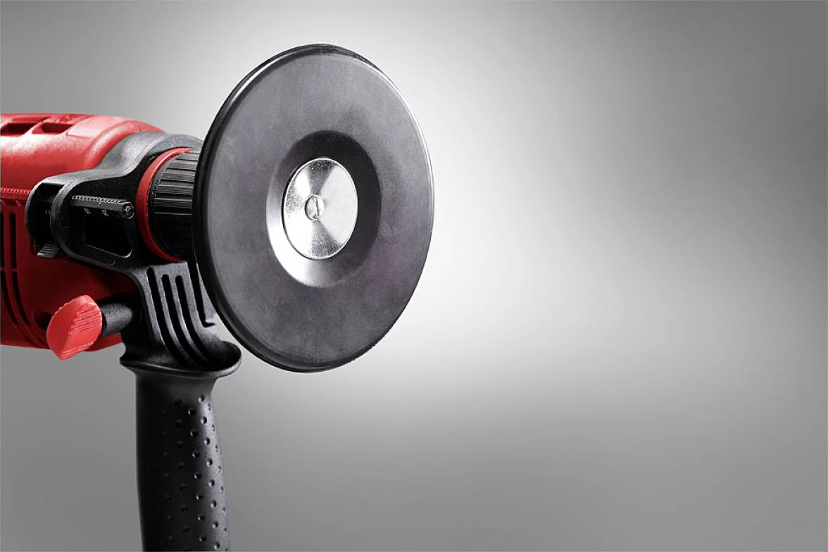 Rdeče električno orodje s črnim ročajem in rotirajočo ploščico, verjetno brusilnik, na sivi podlagi.