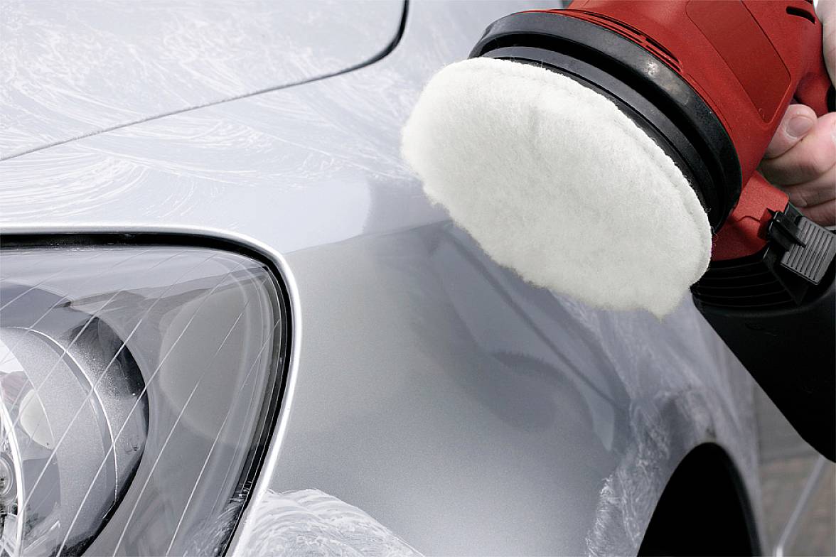 Rdeča polirna naprava polira srebrno barvo avtomobila, na kateri so ostanki mila. Avtomobil je delno viden.