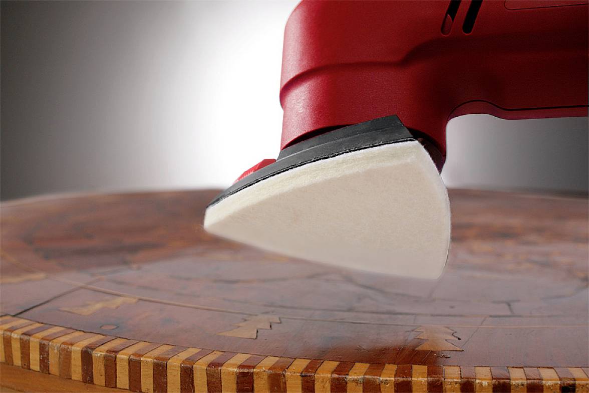 Rdeč likalnik drsi čez okroglo leseno površino z vloženim vzorcem in simbolizira skrbnost pri negi pohištva.