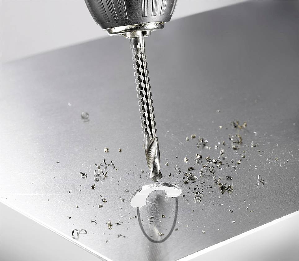 Električni vrtalnik izvrtava luknjo v kovinski plošči. Nekaj kovinskih odrezkov je razpršenih okoli luknje.