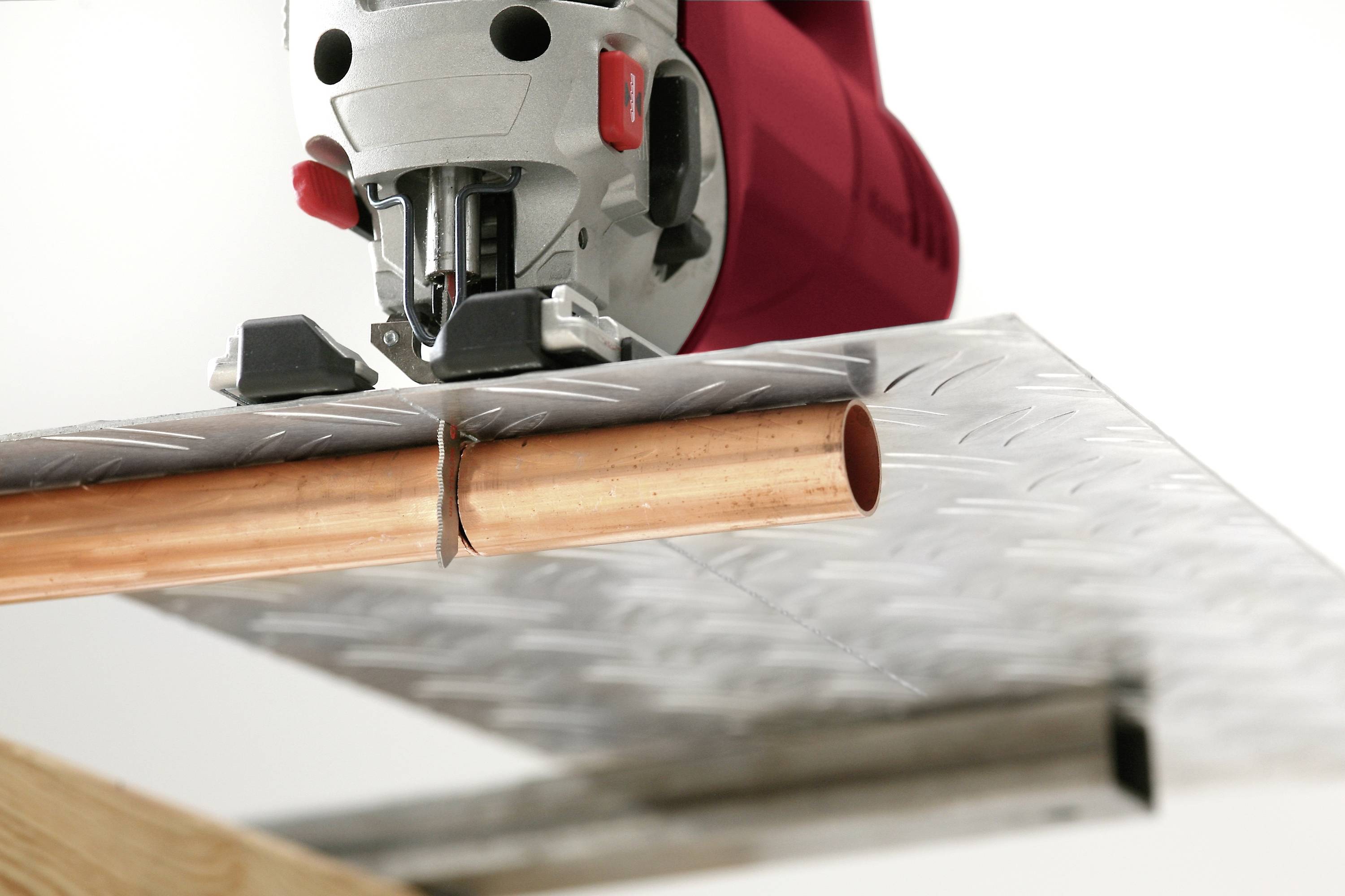 Vbodna žaga reže bakreno cev na kovinski plošči, kar prikazuje natančen rez.