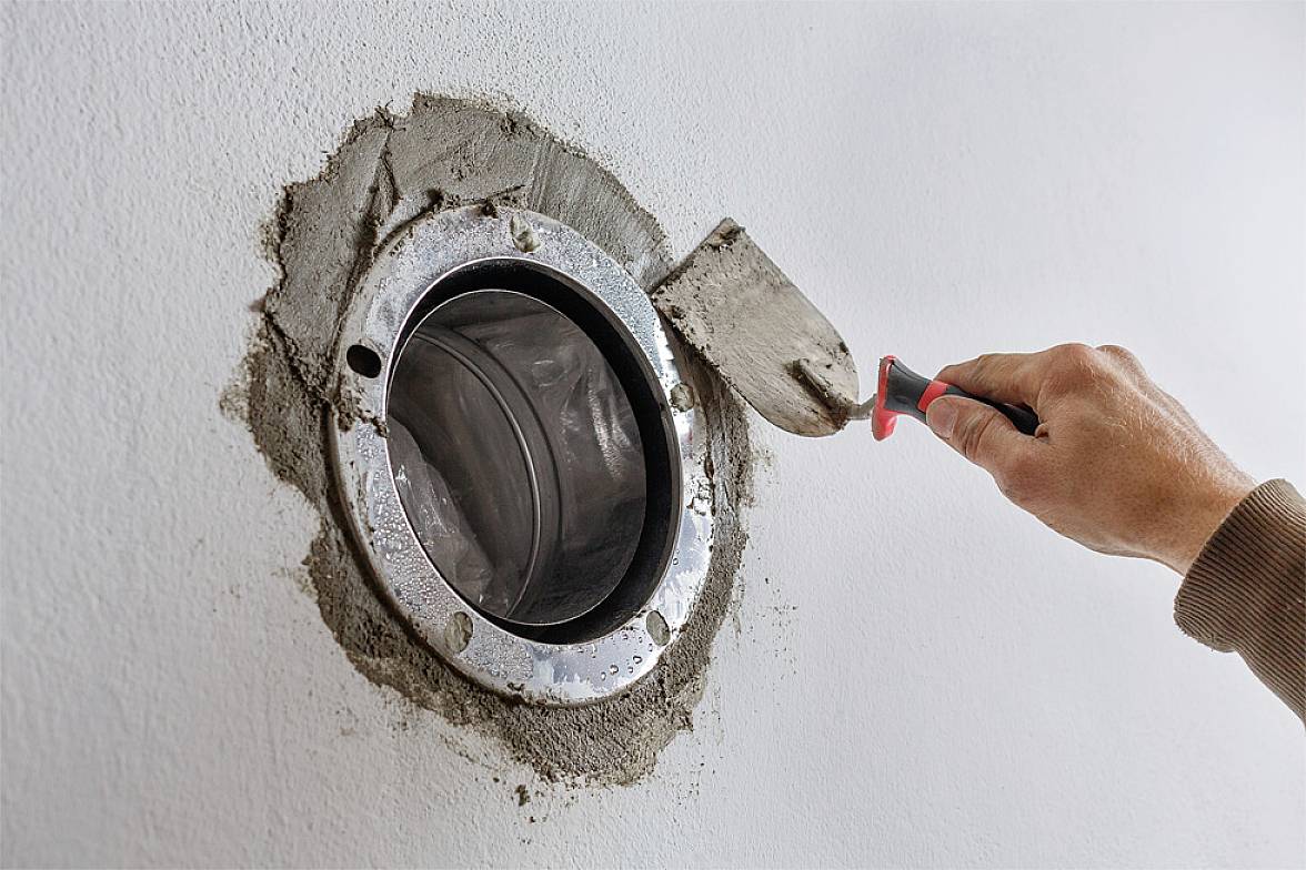 Oseba z ravno zidarsko gladilko poravnava svež cement okoli okroglega stenskega cevi.