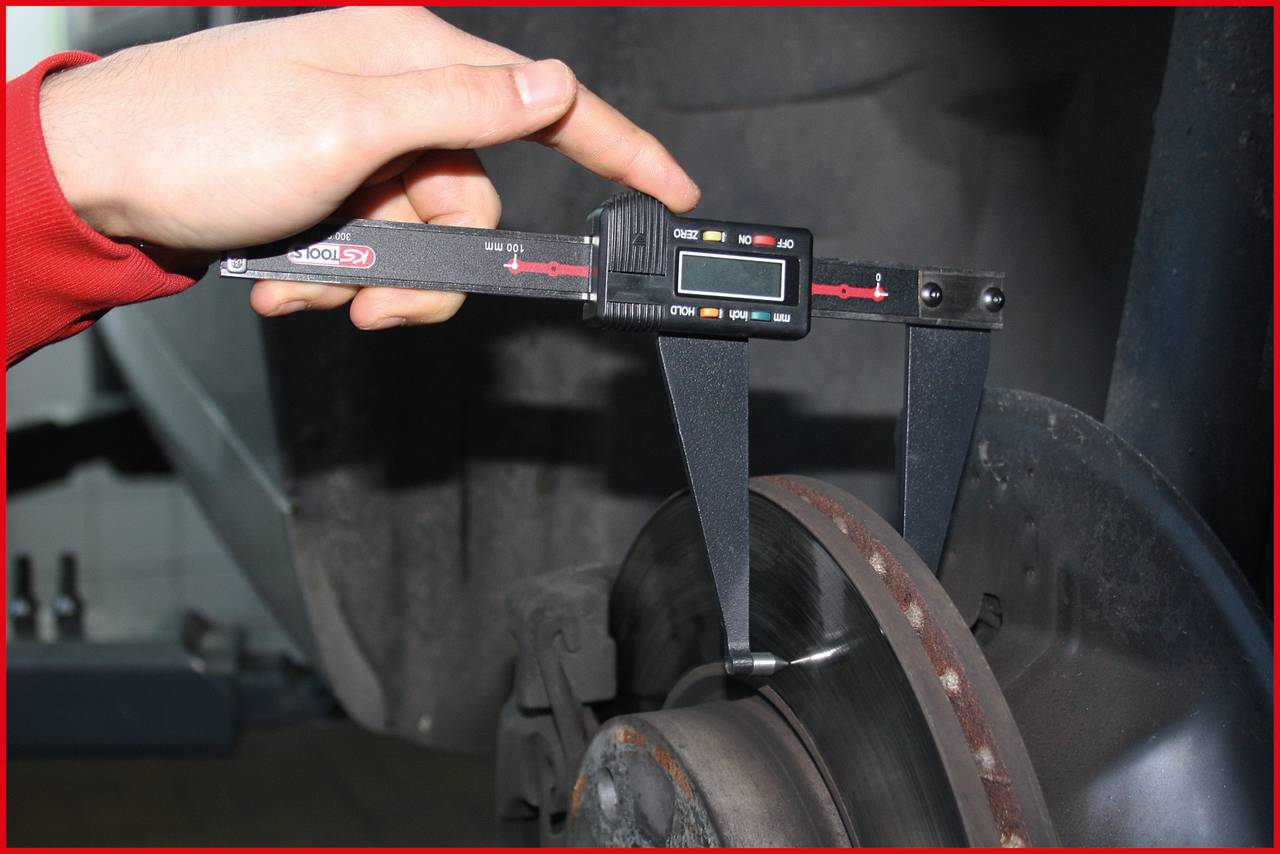 Oseba meri debelino zavorne plošče z digitalnim kljunastim merilom, da bi preverila obrabo dela.