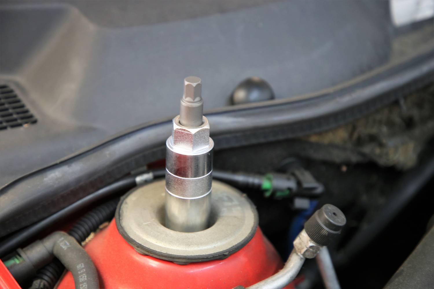 Bližnji posnetek blažilnika v motornem prostoru vozila, ki prikazuje zgornji konec in montažne komponente.