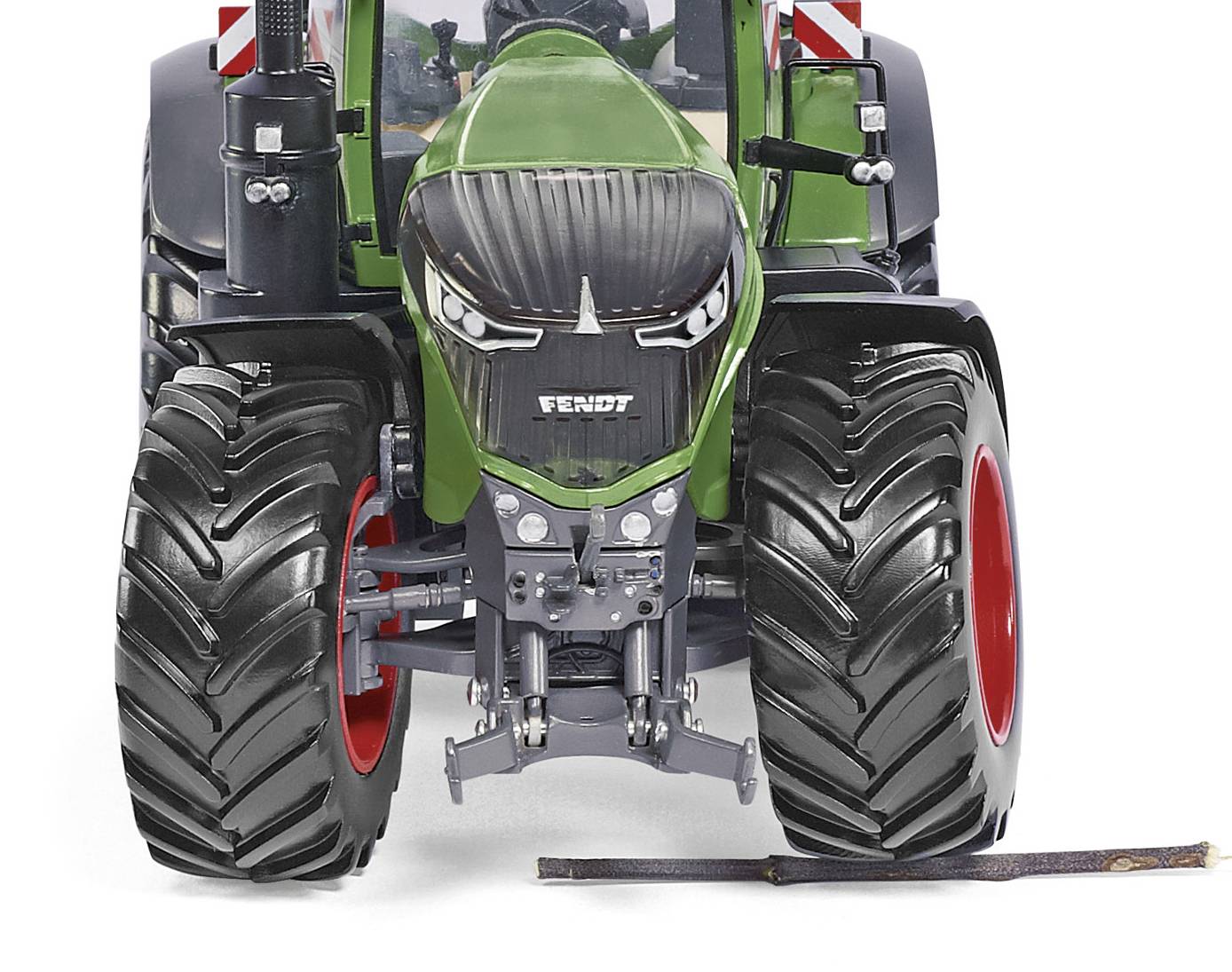 Zelen traktor z velikimi črnimi kolesi stoji na cesti. Pred traktorjem leži majhna veja.