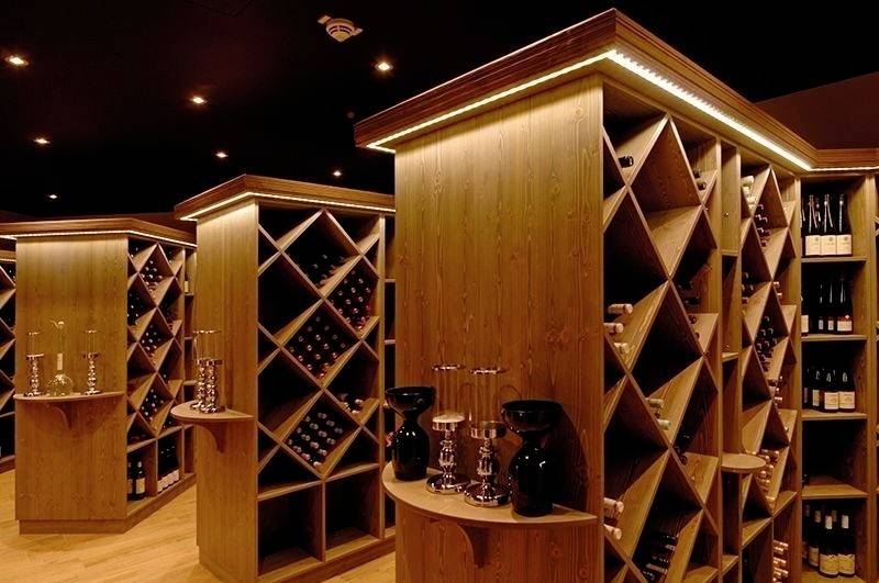 Vinska klet z leseno opremo, osvetljena. Police z policami, opremljenimi z vini. Elegantne dekoracije, vključno s svečniki.