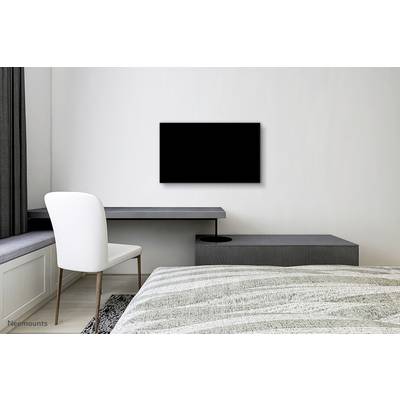 Minimalistična spalnica z posteljo, pultom in stolom ob oknu ter črnim televizorjem na steni.