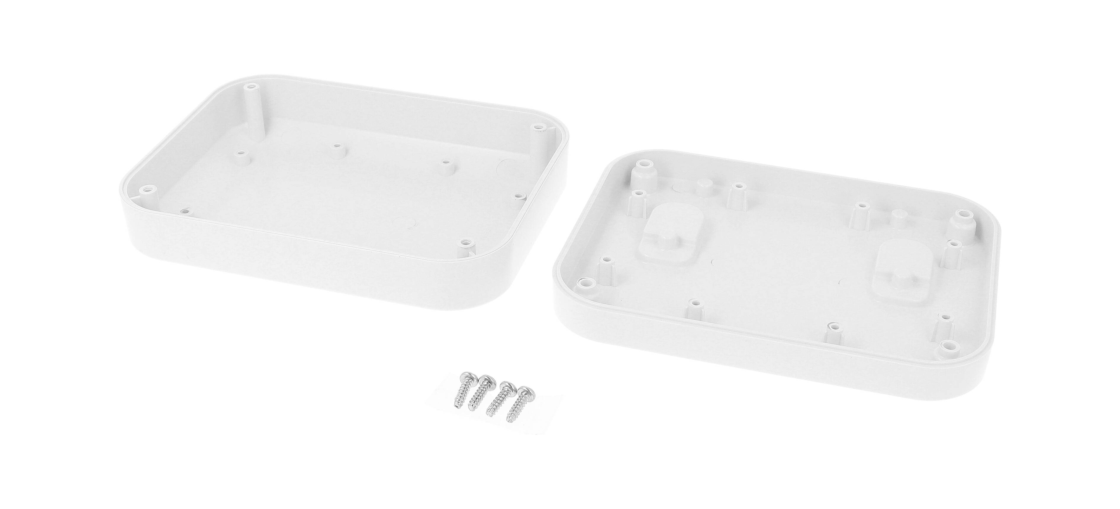 Dve beli plastični polovici ohišja z zaobljenimi robovi, ločeni druga od druge in ležeči na tleh, spremljani s štirimi vijaki.