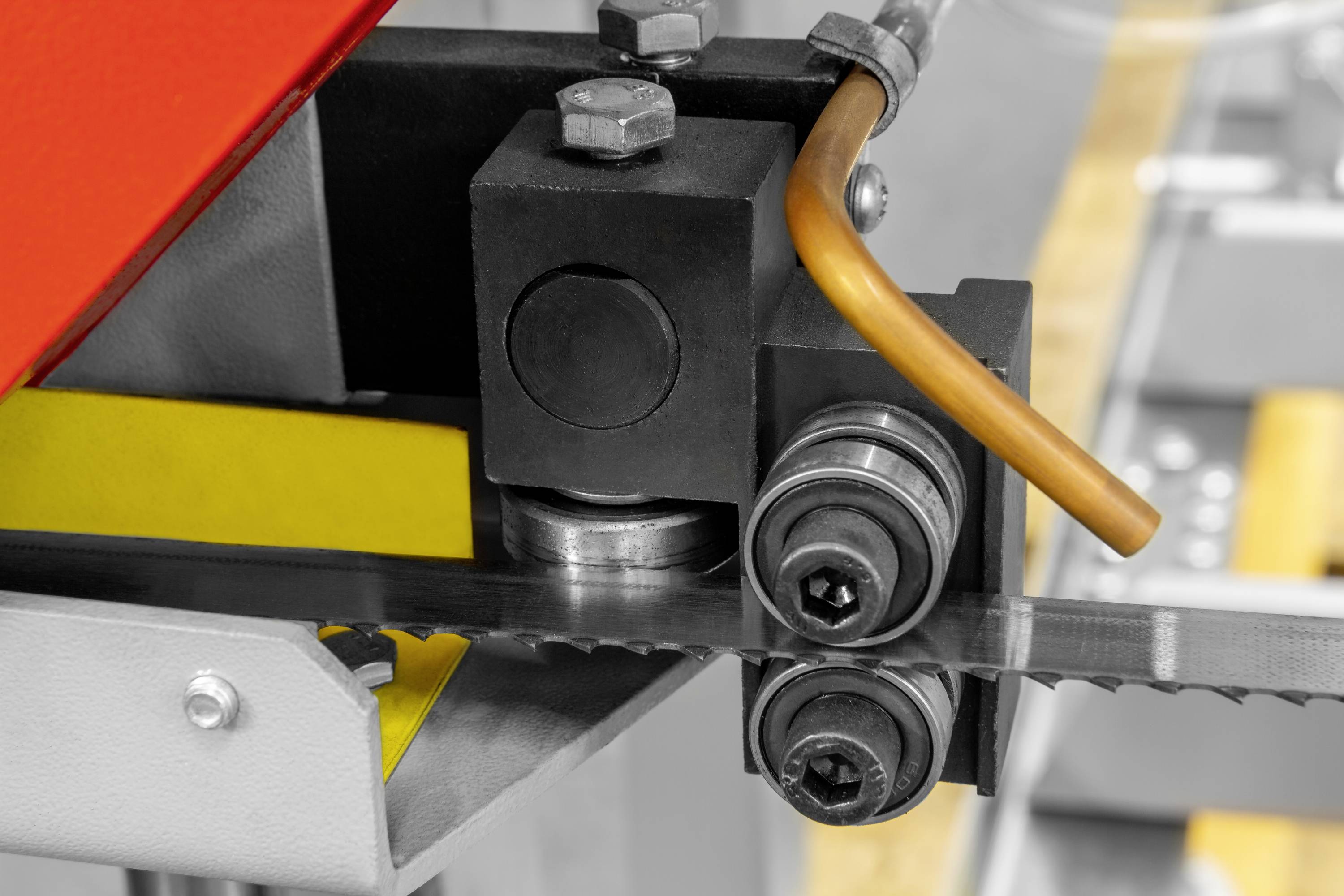 Bližnji posnetek tračne žage z kovinsko vodilno tirnico. Vidno rumeno zaščitno ohišje in oranžni kabli.