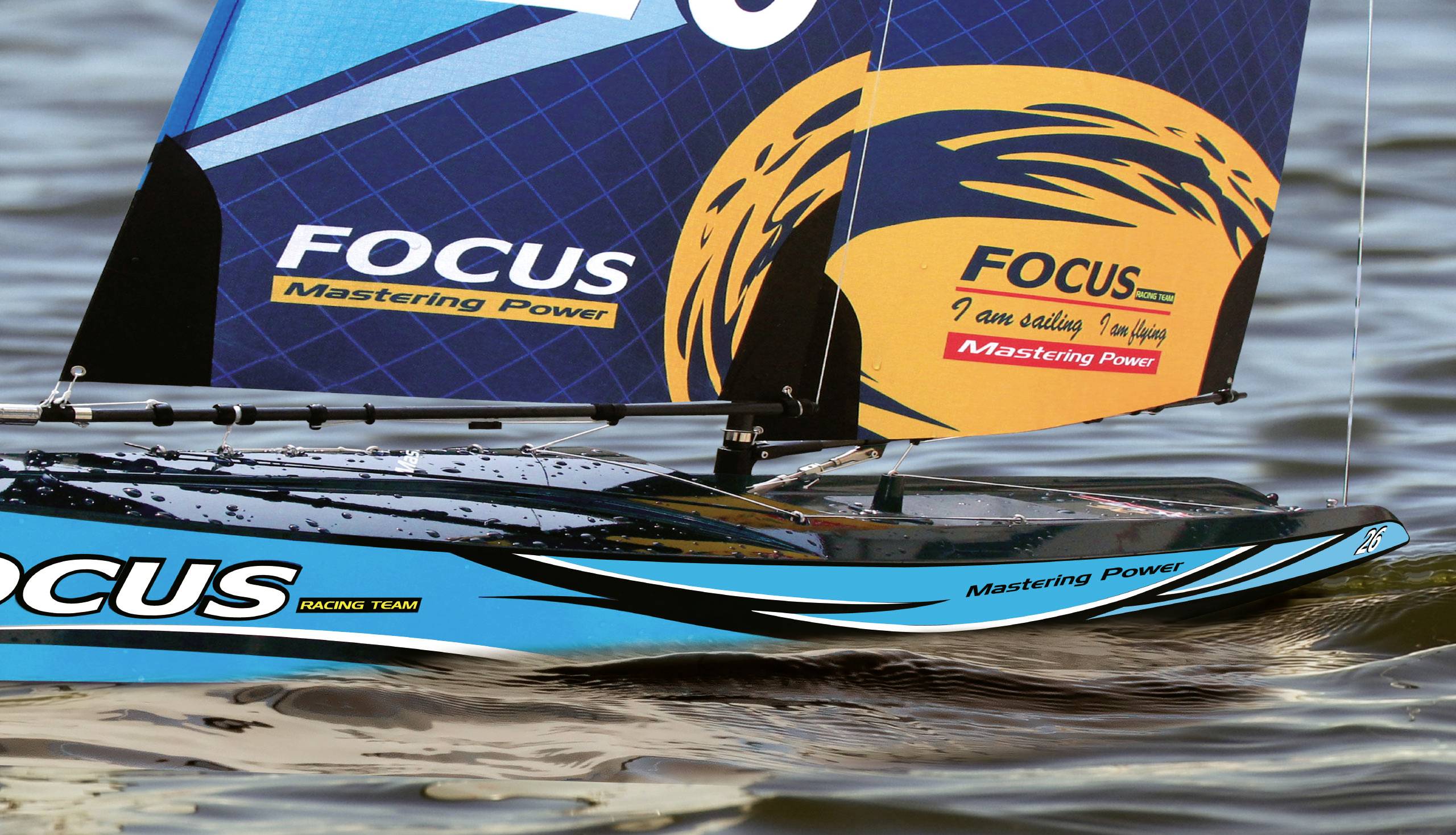 Modri modelarski jadralni čoln na vodi z napisom »FOCUS Mastering Power« na jadru.