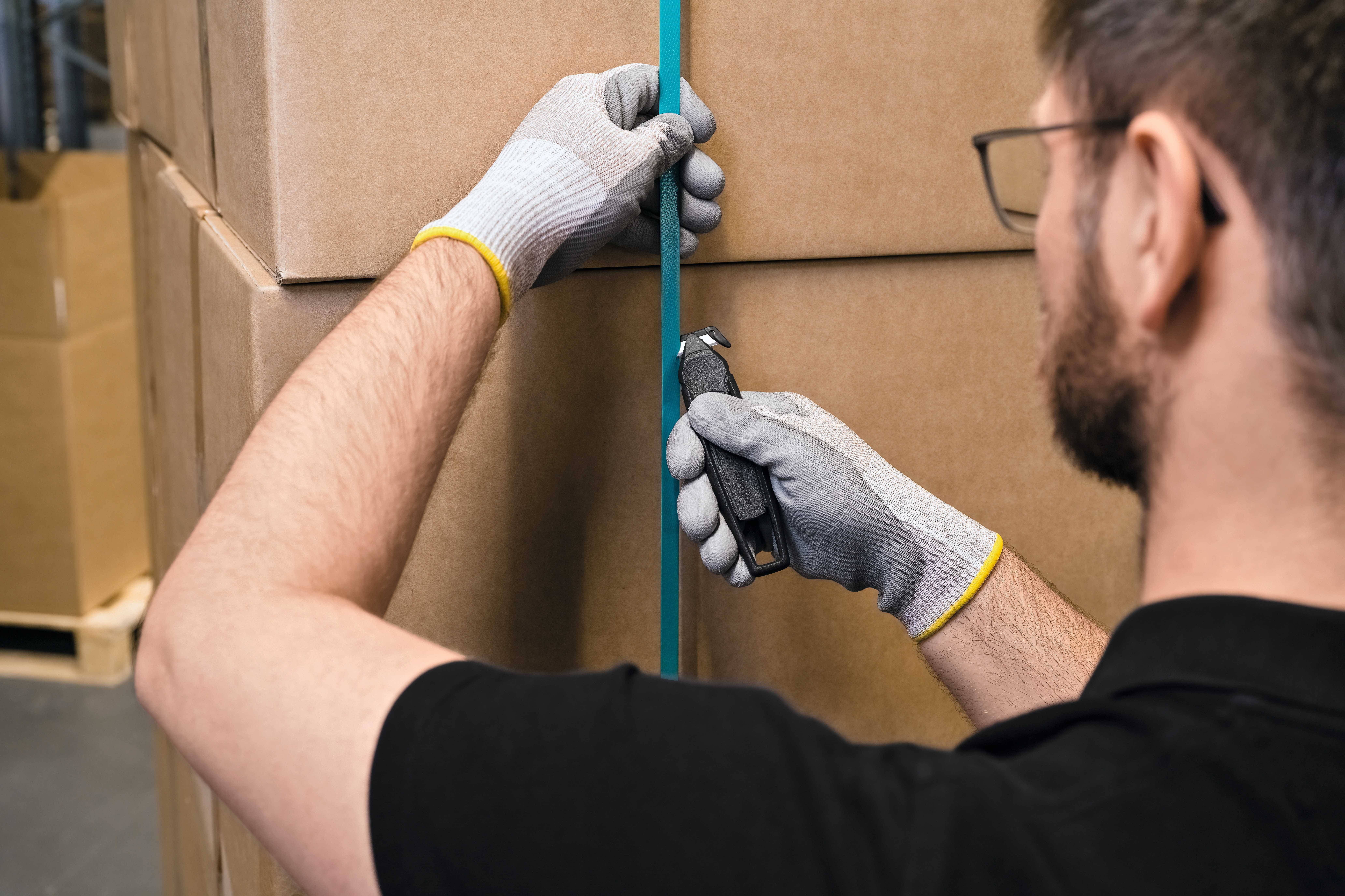 Oseba v rokavicah z rezalnim nožem odpira paket, ki je ovit z modrim trakom.