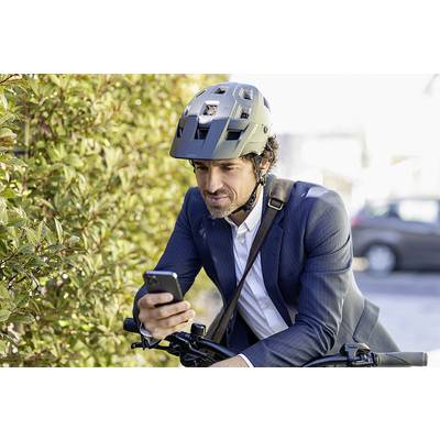 Moški v obleki, ki nosi čelado in drži pametni telefon, medtem ko sedi na kolesu ob živi meji ob cesti.