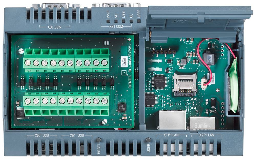 Odprta elektronska naprava z zelenimi priključnimi letvami na levi strani in tiskanim vezjem z različnimi priključki na desni strani.