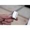 Ena roka drži srebrn, kovinski nastavek, verjetno orodje. Ozadje je zamegljeno in prikazuje delovno površino.