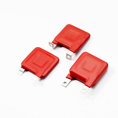 Tri rdeče, kvadratne električne komponente z kovinskimi kontakti na beli podlagi.
