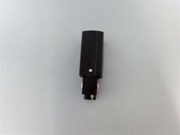 Črn adapter na sivi podlagi, verjetno električni ali avdio adapter, postavljen pokončno.