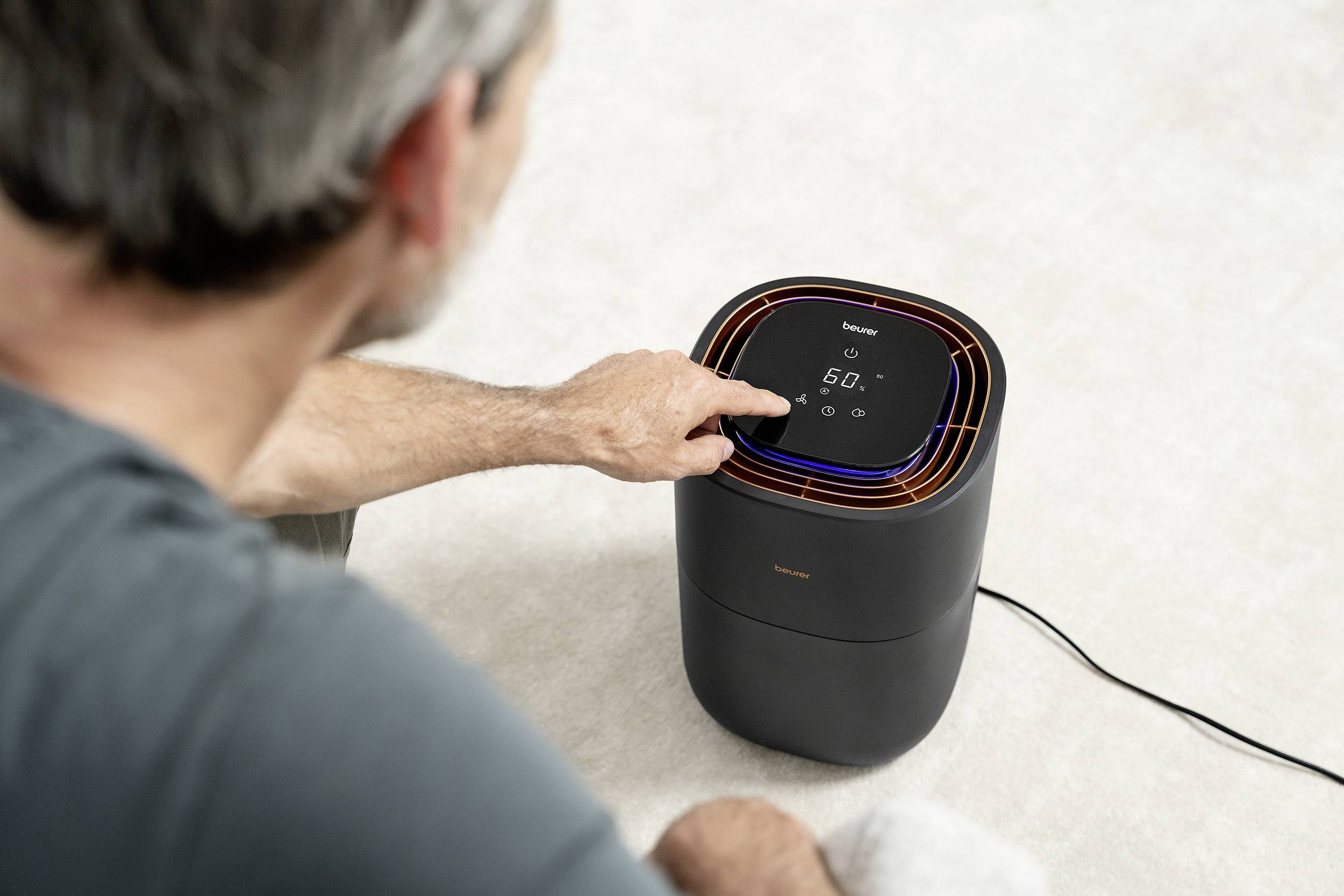 Oseba upravlja kompaktno, črno napravo z zaslonom in na dotik občutljivimi tipkami, verjetno čistilec zraka ali ventilator.