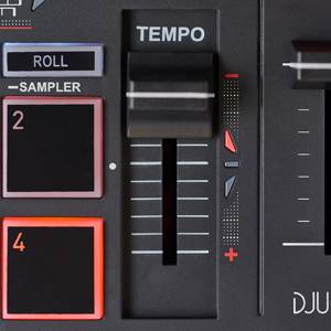 Izrez DJ mešalne mize z drsniki za 'tempo' in tipkami za 'sampler'. Vidni so osvetljeni zasloni in številke.