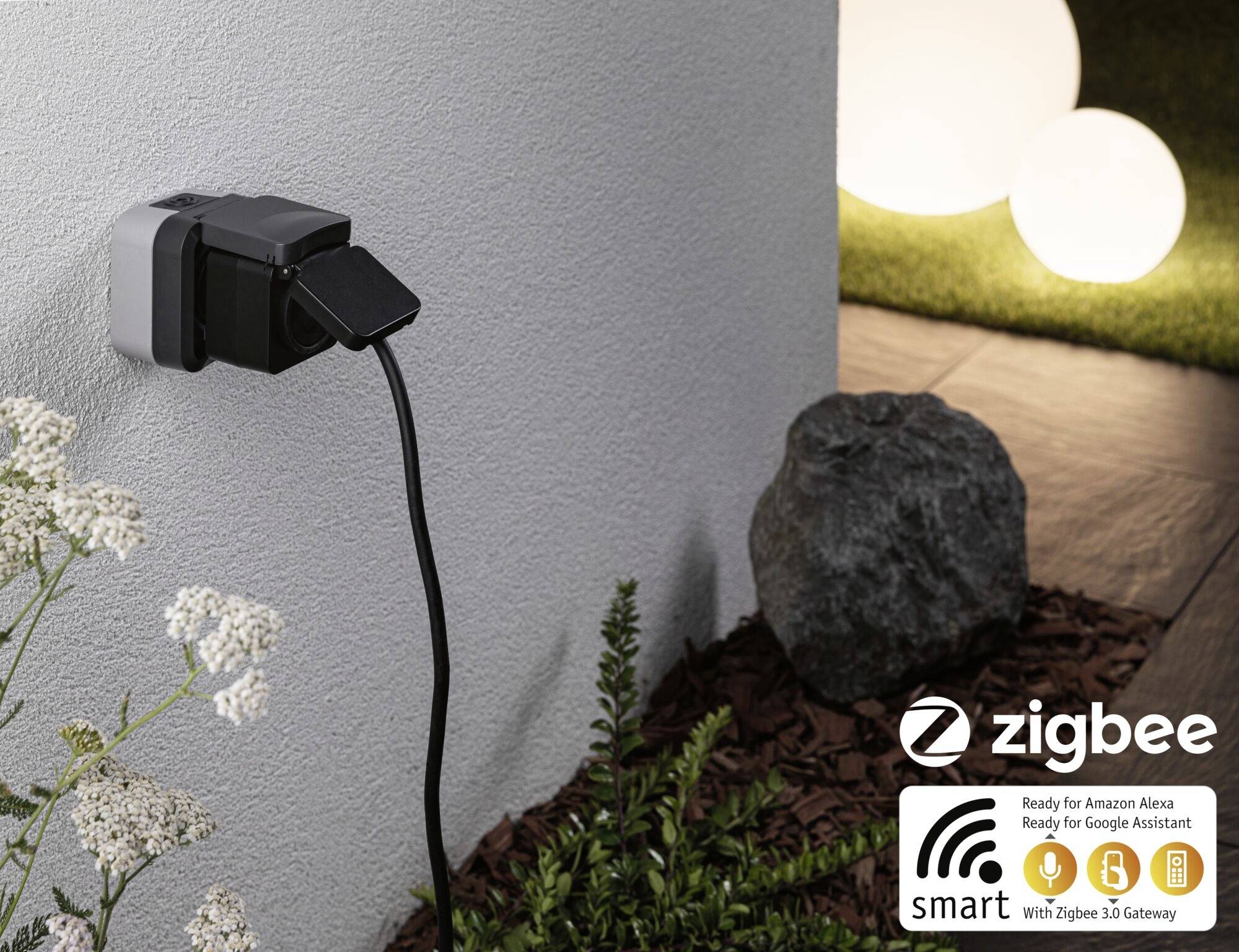 Zunanja električna vtičnica s priključenim napravnim kablom. Logotip 'zigbee' spodaj desno, prikazuje združljivost z Alexo in Google Assistantom.