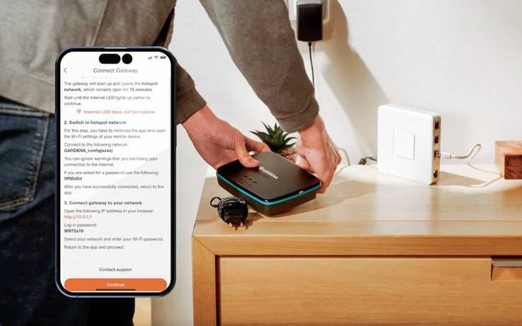 Oseba, ki drži napravo za namestitev Wi-Fi ob leseni površini, sledi navodilom za namestitev na zaslonu pametnega telefona.