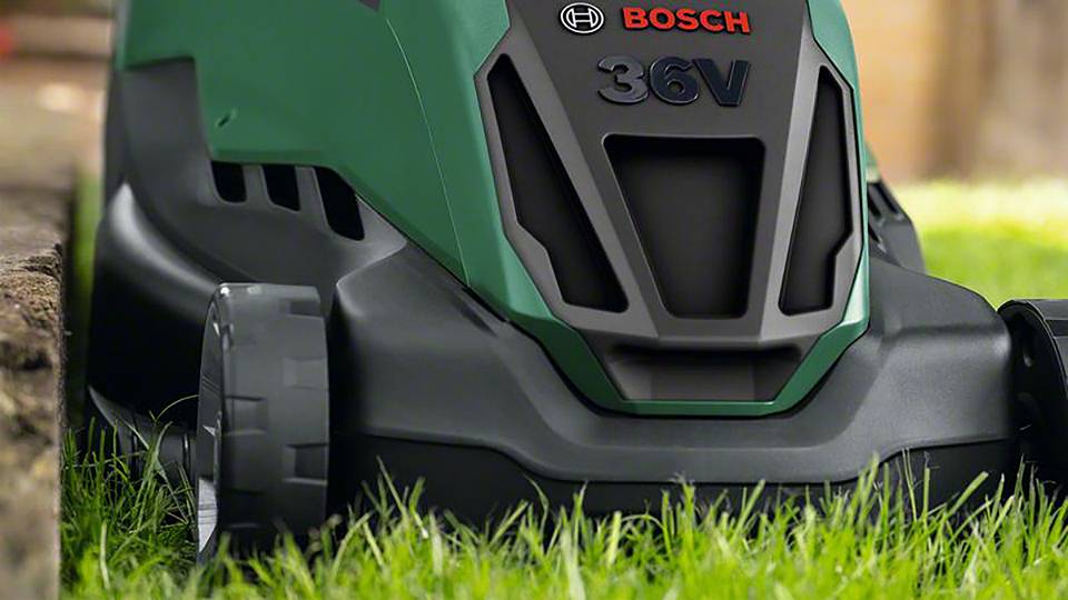 Zelen električni kosilnik kosi travo na vrtu. Na kosilniku piše 'BOSCH 36V'.