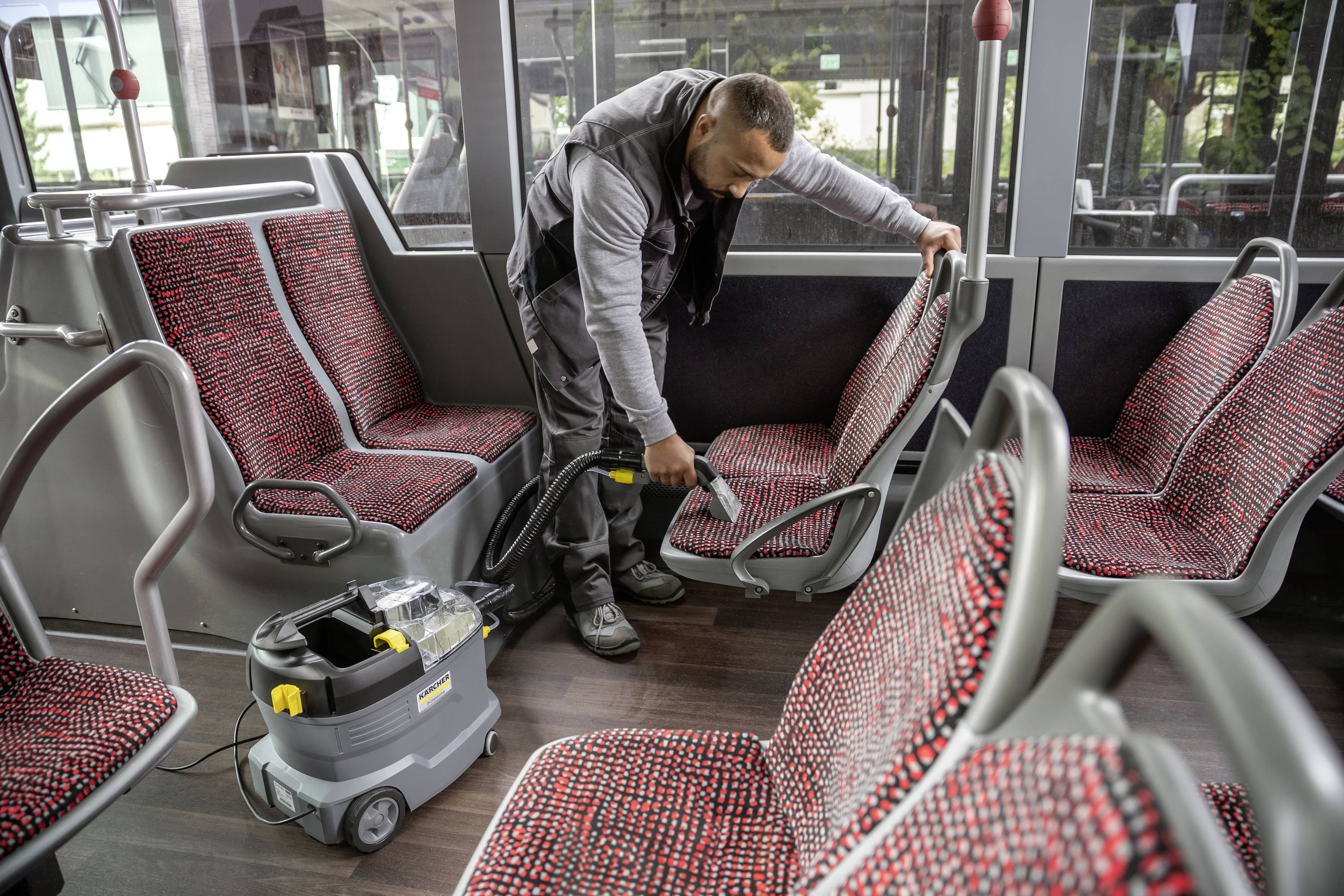 Moški čisti sedeže v praznem avtobusu z sesalnikom. Tla in sedeži so čisti in dobro vzdrževani.