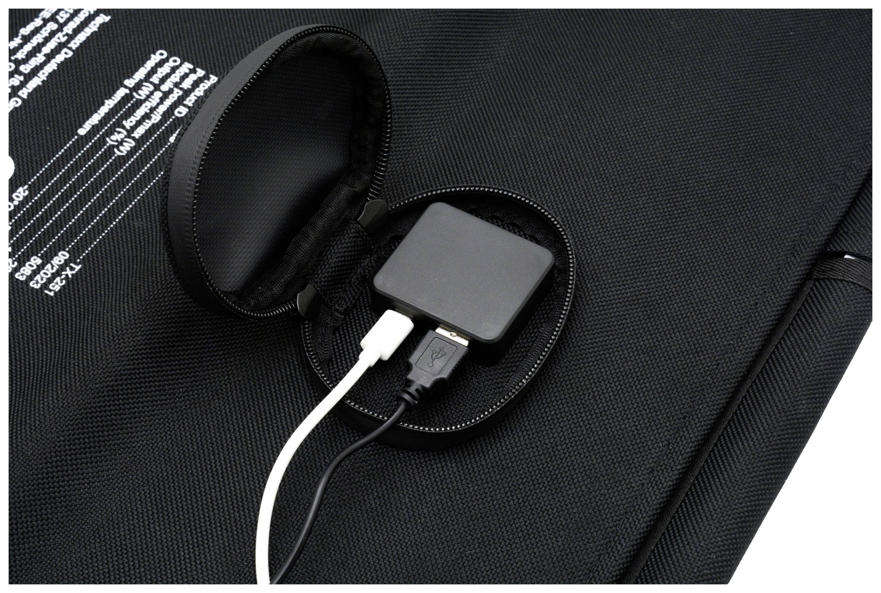 Črna naprava z dvema USB-kabloma, enim belim in enim črnim, je priključena in leži na črnem tekstilnem ozadju.