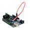 Arduino plošča s priključenim kamerinim modulom. Rdeči kabli povezujejo komponente, ki ležijo na beli podlagi.